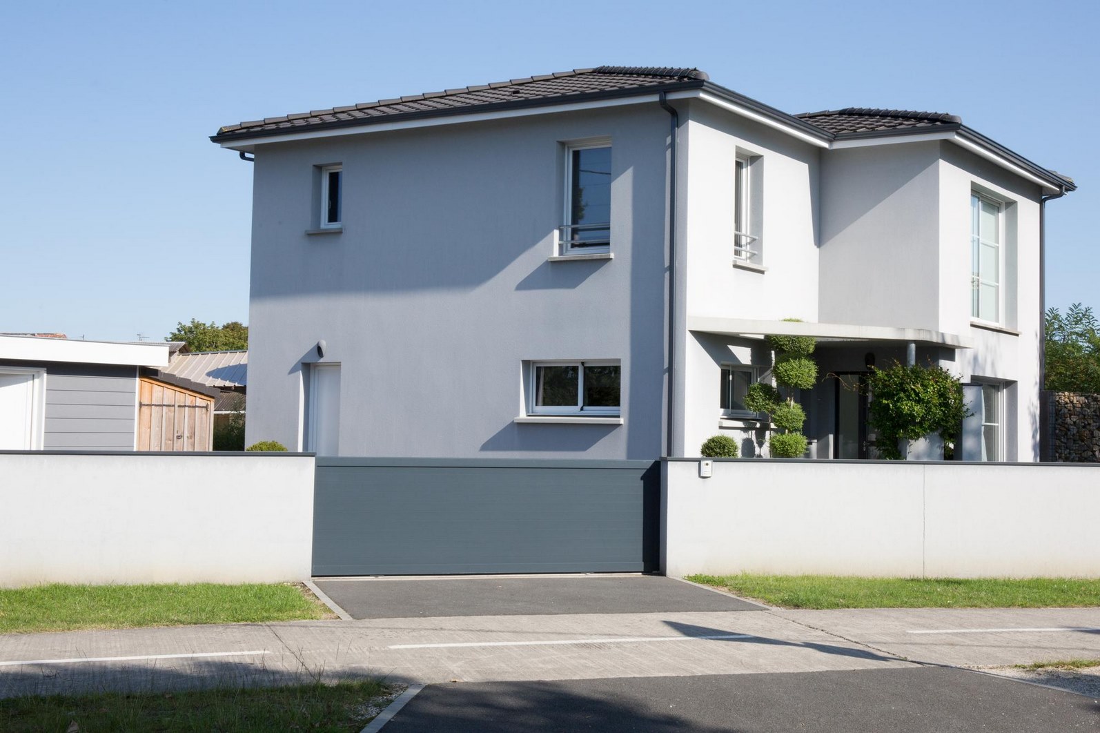 Menuiseries PVC, bois et aluminium : portails, volets, portes et fenêtres sur mesure Vue d’ensemble d’un extérieur avec différentes menuiseries : un portail en aluminium anthracite, des volets battants en bois clair, des fenêtres en PVC blanc à double vitrage, et une porte d’entrée en alu au design contemporain. Chaque élément met en valeur la diversité des matériaux et des finitions disponibles pour l’habitat.